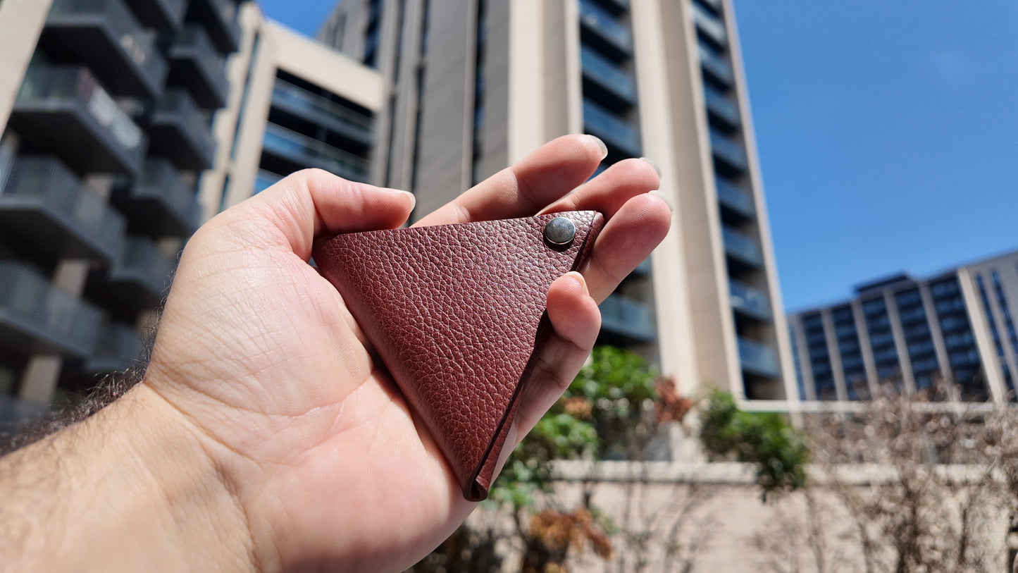 Close-up of a handmade auburn leather coin pouch photographed outdoors in natural daylight.