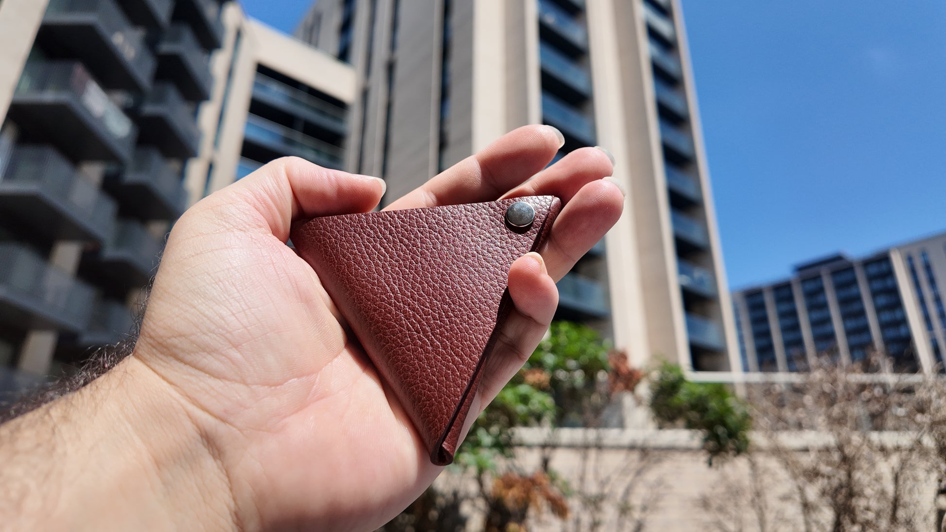 Close-up of a handmade auburn leather coin pouch photographed outdoors in natural daylight.