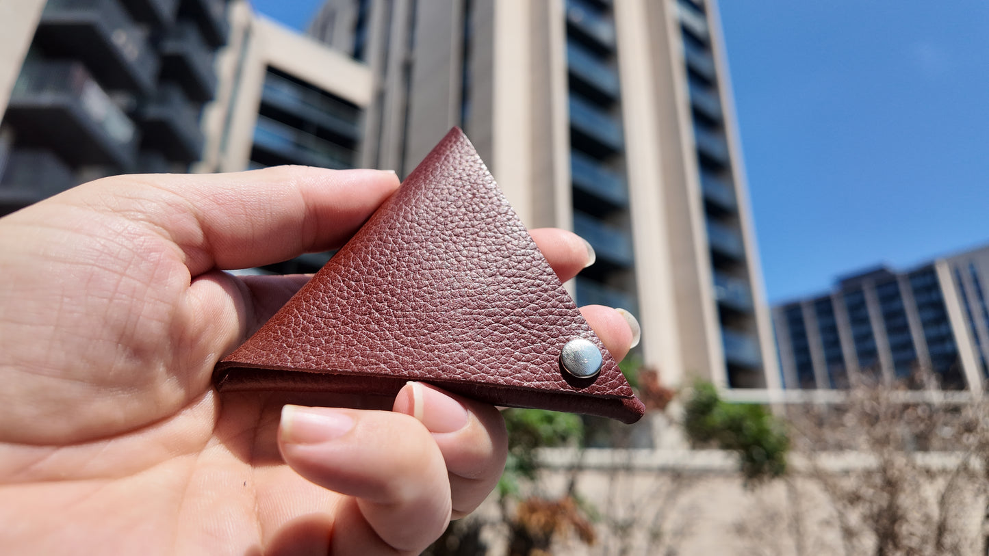 Front close-up of a handmade auburn leather coin pouch showcasing its minimalist triangular design.