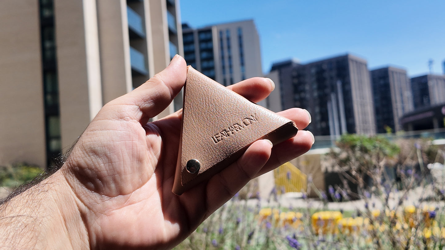 Beige leather coin pouch held outdoors with a modern city skyline in the background
