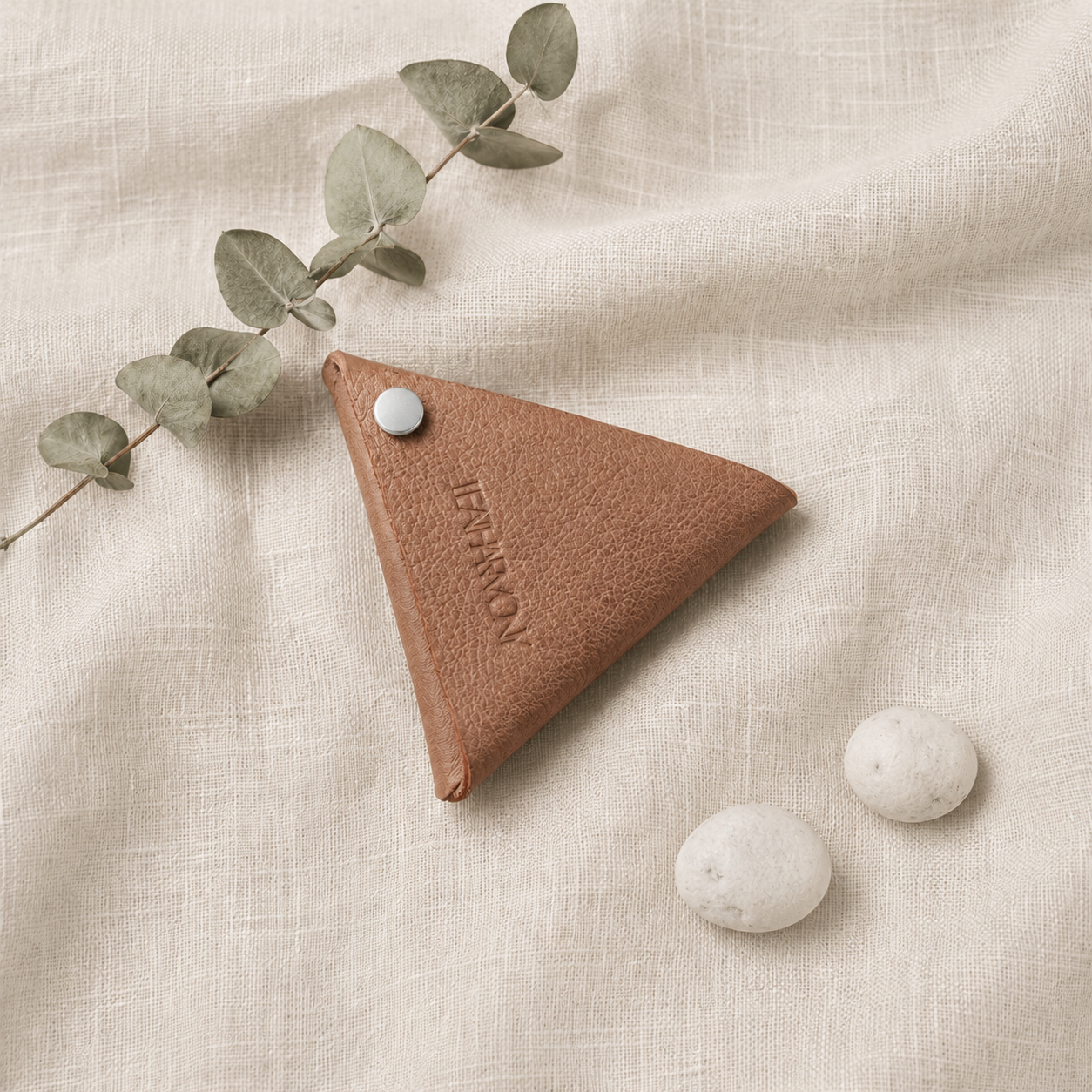 Beige leather coin pouch styled on natural linen fabric with eucalyptus leaves and white stones
