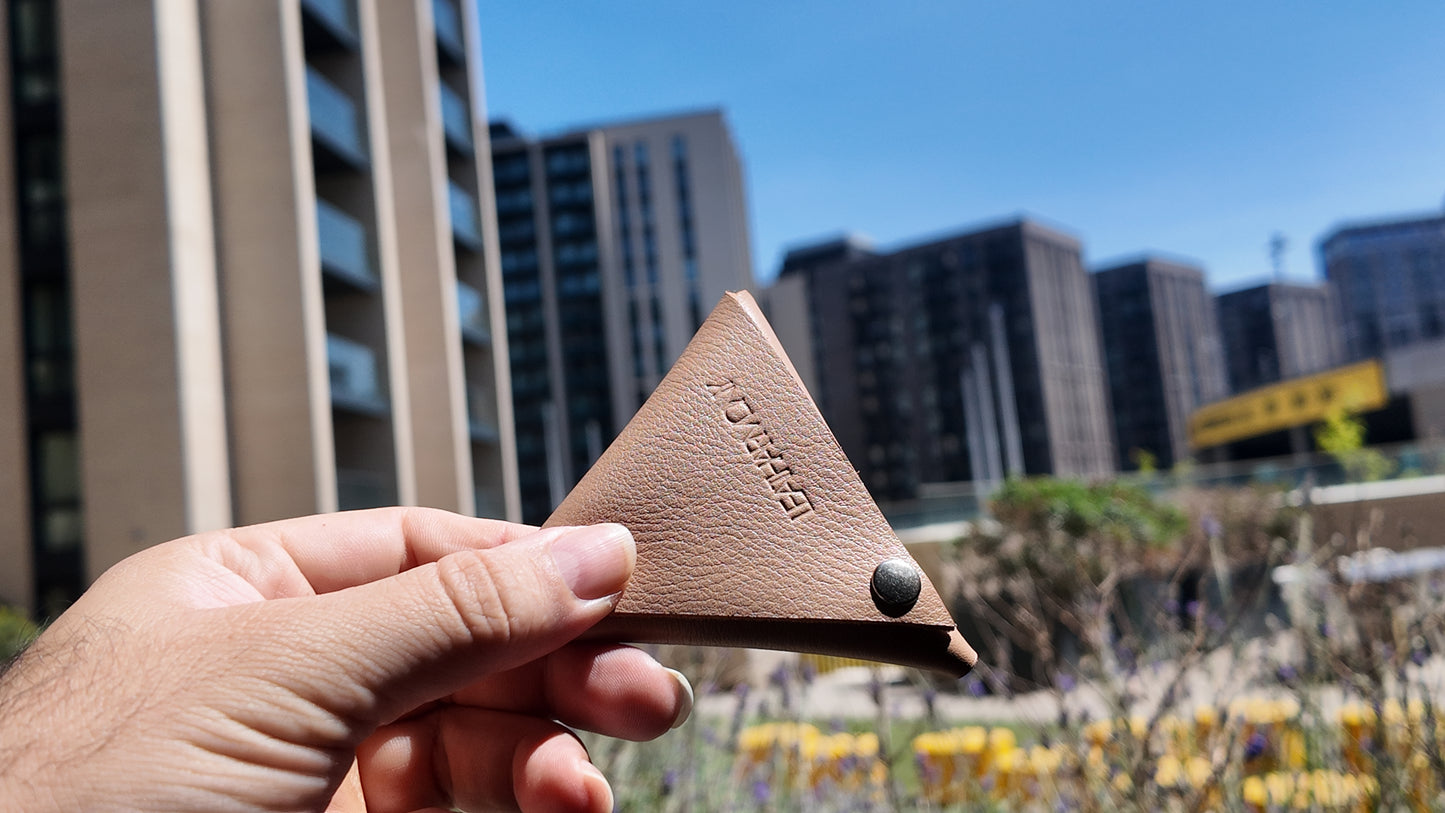 Beige leather coin pouch held by hand with a contemporary cityscape in the background
