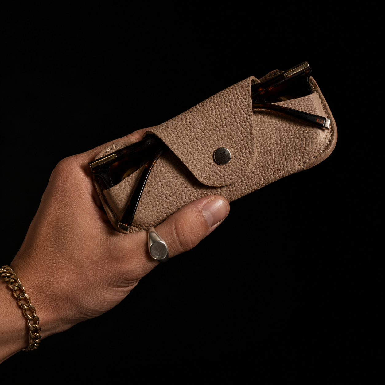 Close-up of a handmade beige leather eyewear case held by hand against a black editorial background.