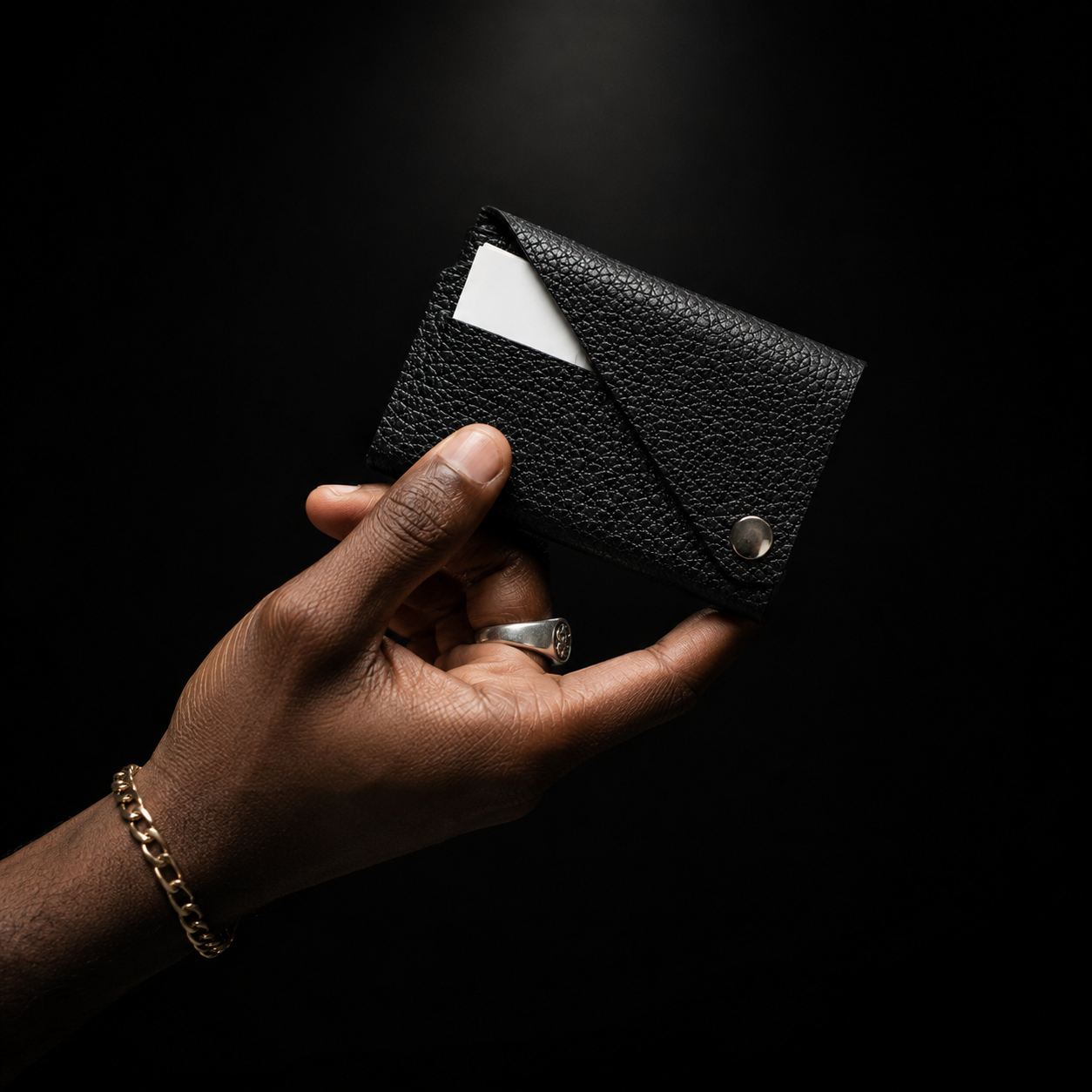 Black leather card holder held in hand against a black background, highlighting its textured leather and silver-tone closure.