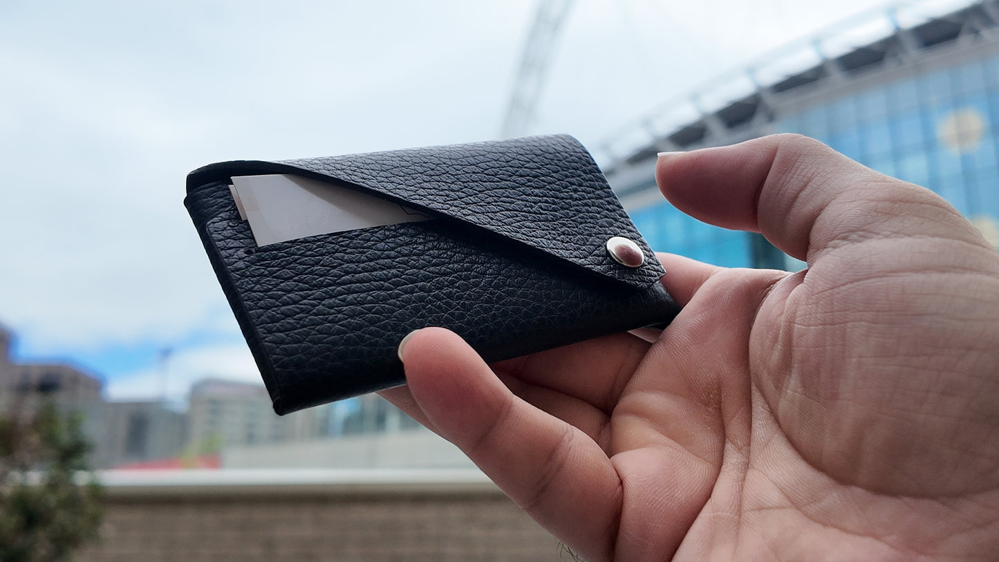Close-up of a black leather card holder held in hand, highlighting its textured finish and minimalist design.