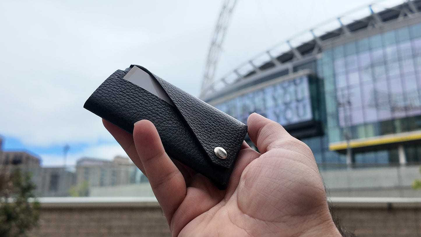 Black leather card holder held in hand outdoors, showing its compact envelope construction.