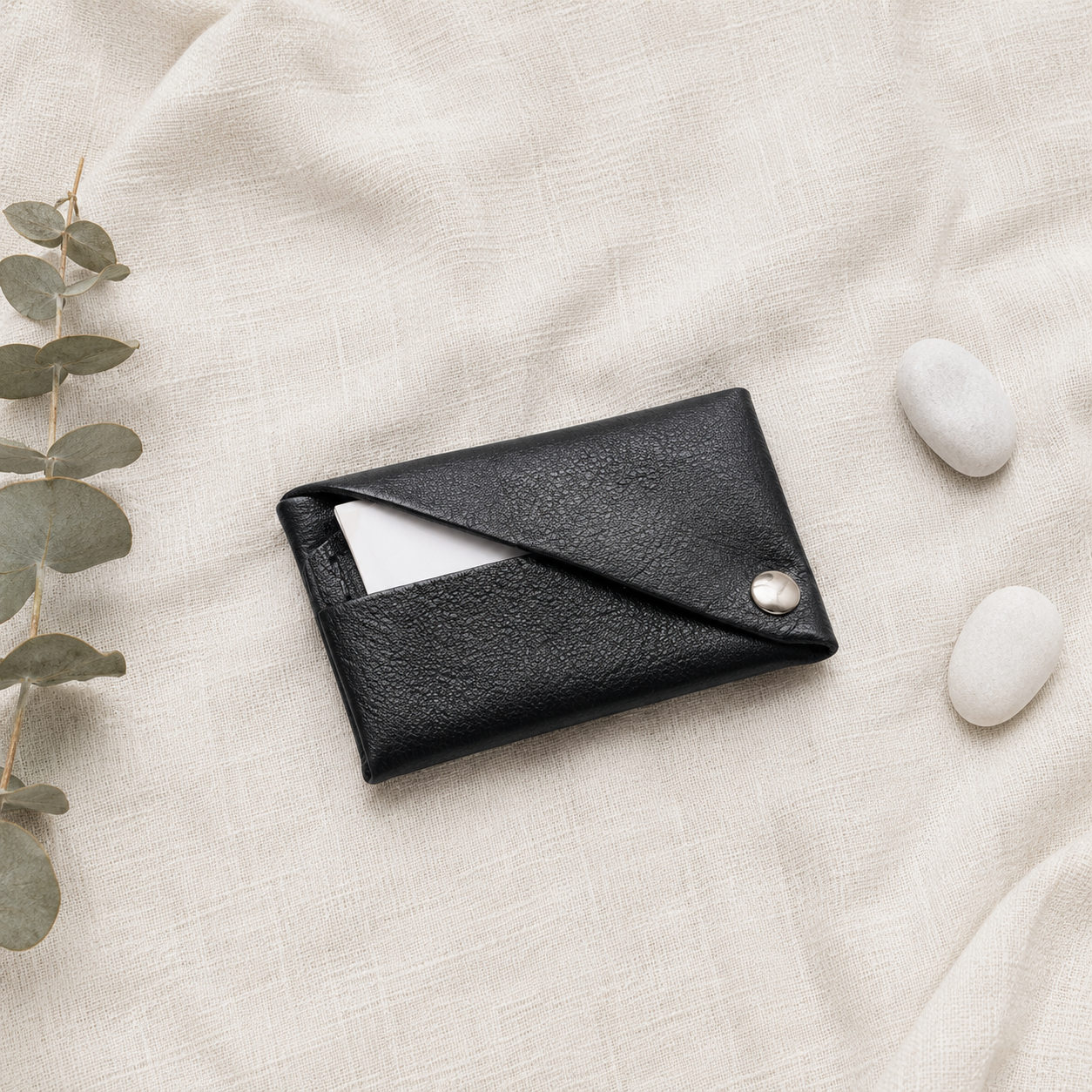 Black leather envelope card holder styled on neutral linen with eucalyptus and white stones