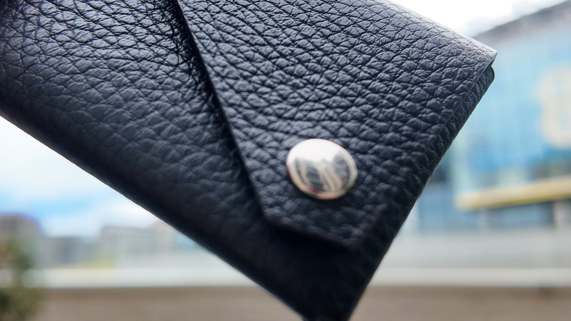 Close-up of a black leather card holder highlighting its textured leather and silver-tone stud closure.