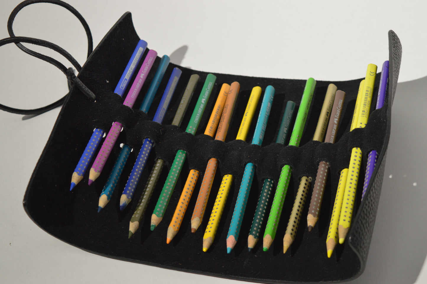 Open black genuine leather pencil case with coloured pencils displayed on a clean white background.