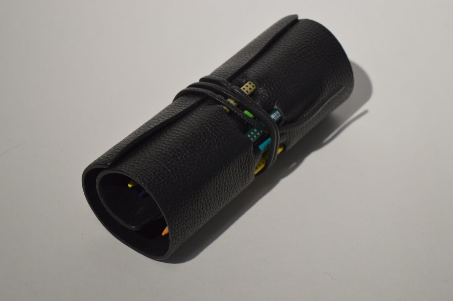 Minimalist black genuine leather pencil case with wrap closure photographed on a clean white background.