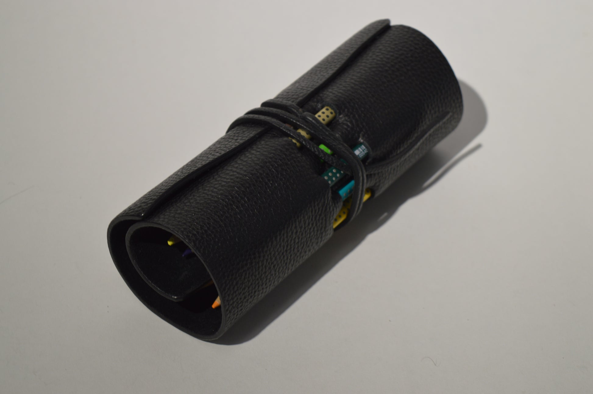 Minimalist black genuine leather pencil case with wrap closure photographed on a clean white background.