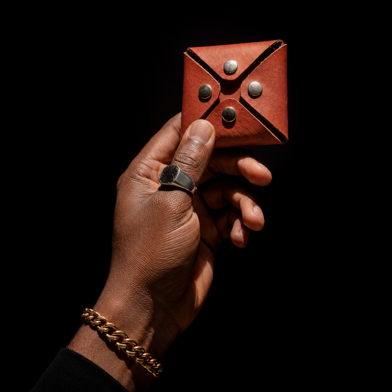 Handmade brown leather coin pouch held against a black background, highlighting its geometric folded design