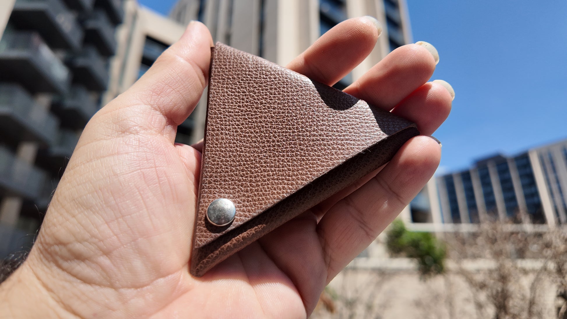 Close-up of a handmade brown genuine leather triangle coin pouch highlighting its pebbled leather texture.