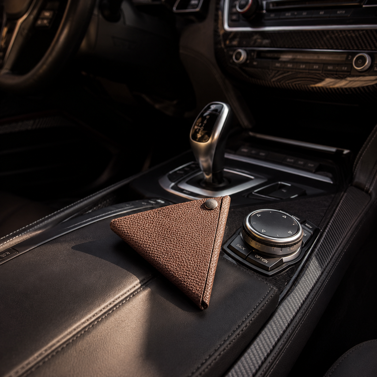Handmade brown leather coin pouch displayed on the centre console of a luxury car interior.