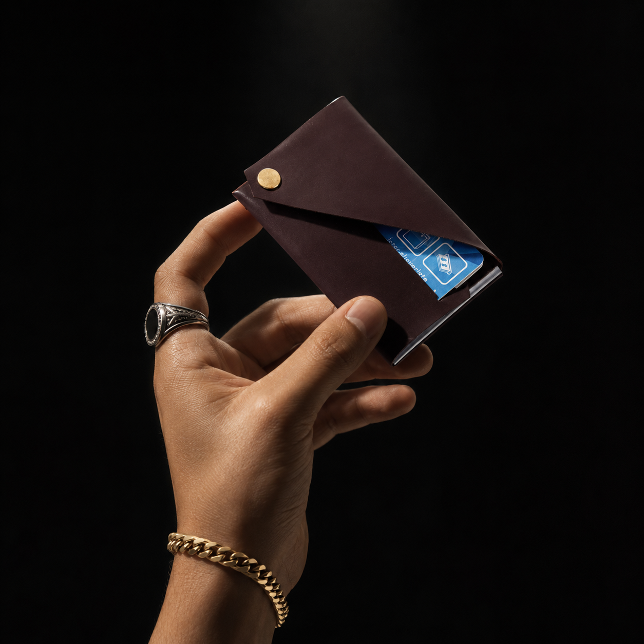 Burgundy patent leather card holder held in hand against a black background, highlighting its envelope design and gold-tone closure.