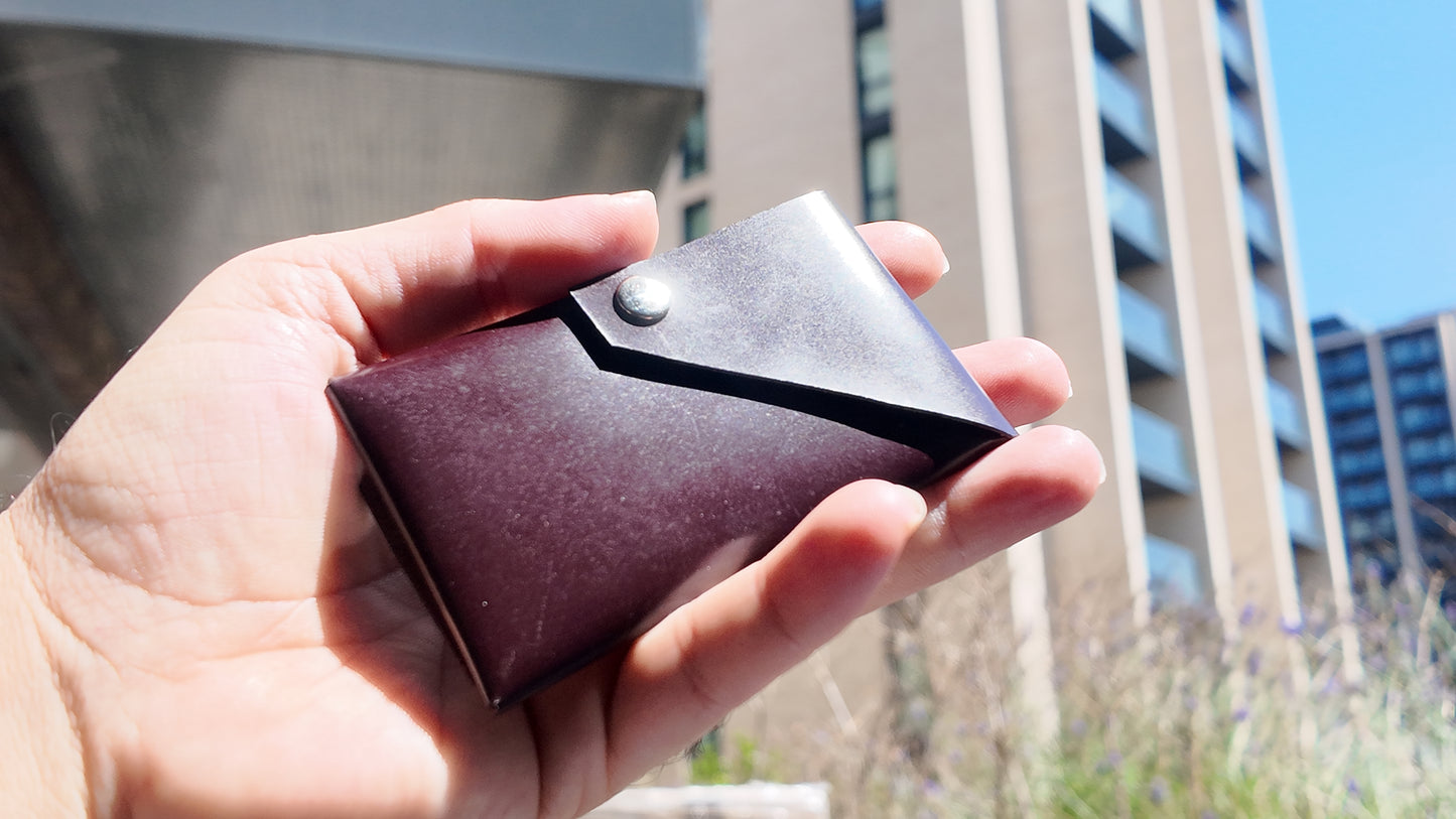 Close-up of a burgundy patent leather card holder held in hand in natural daylight.