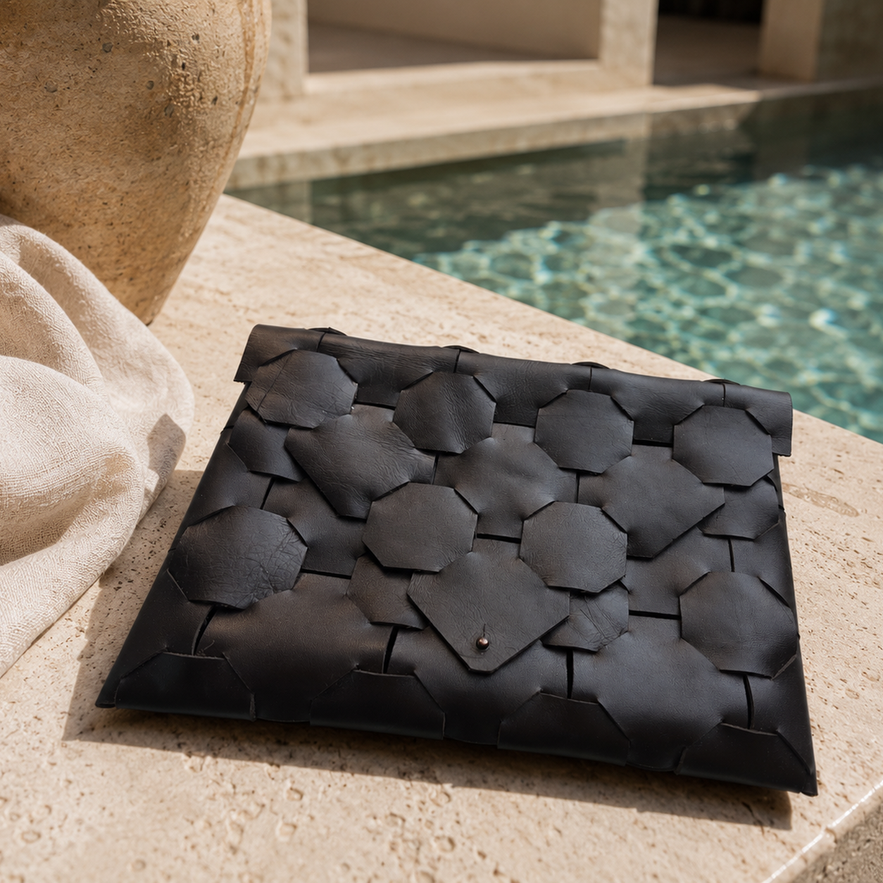 Dark brown woven leather clutch displayed on a stone surface beside a luxury swimming pool.
