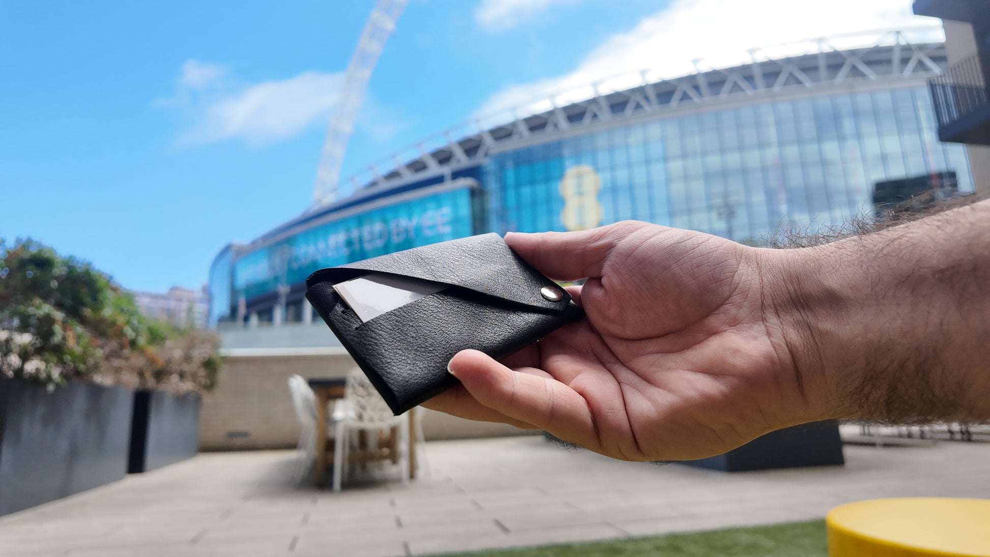 Handmade black genuine leather card holder displayed in hand against a modern city backdrop