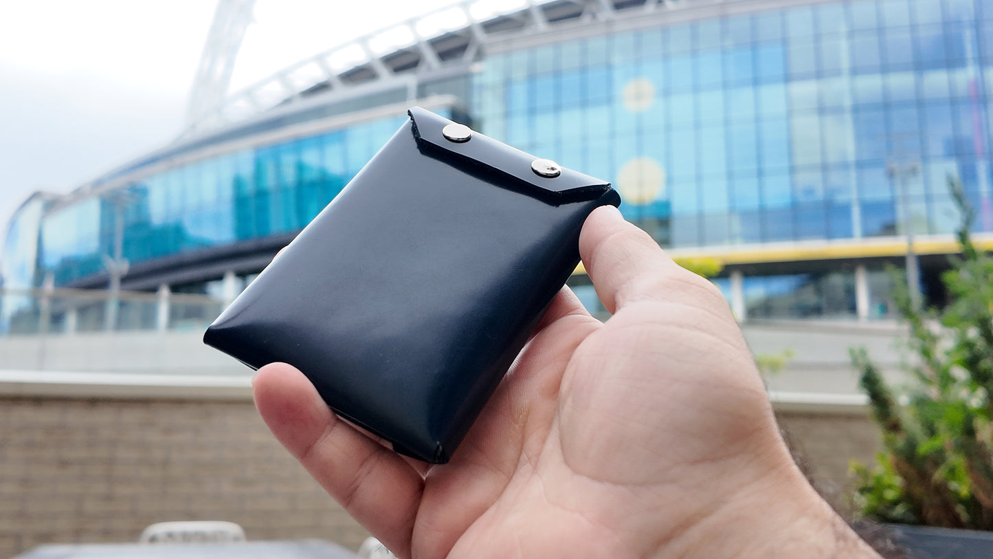 Hand holding back view of a navy wallet with a modern building in the background