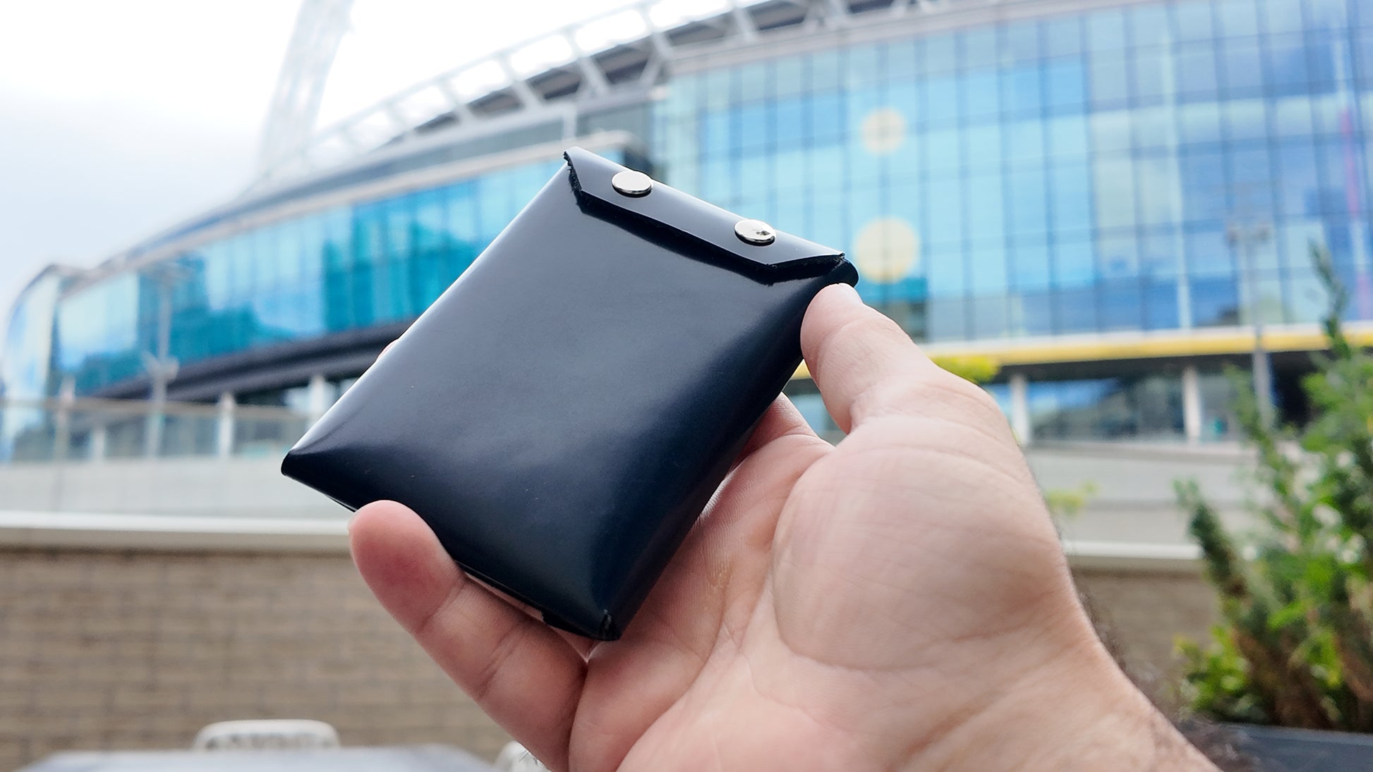 Hand holding back view of a navy wallet with a modern building in the background