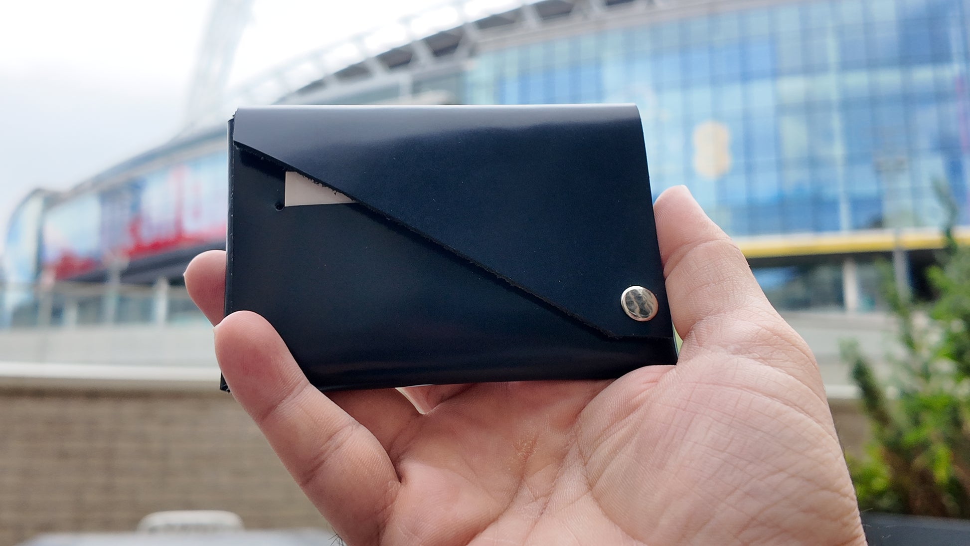 Hand holding a nevy wallet with a metallic snap button against an outdoor background