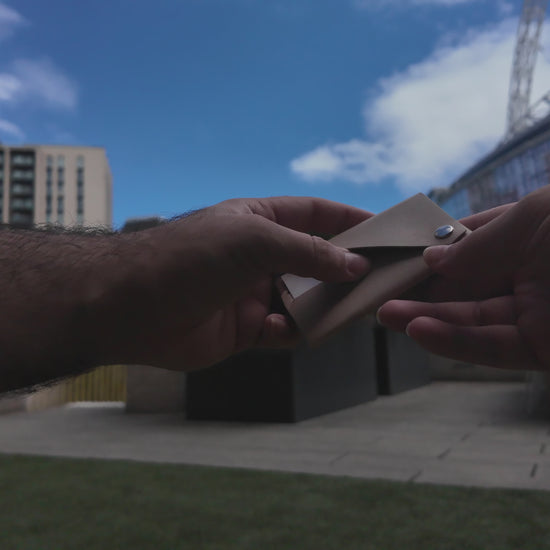 Beige leather envelope card holder demonstrated by hand in an outdoor urban setting near Wembley