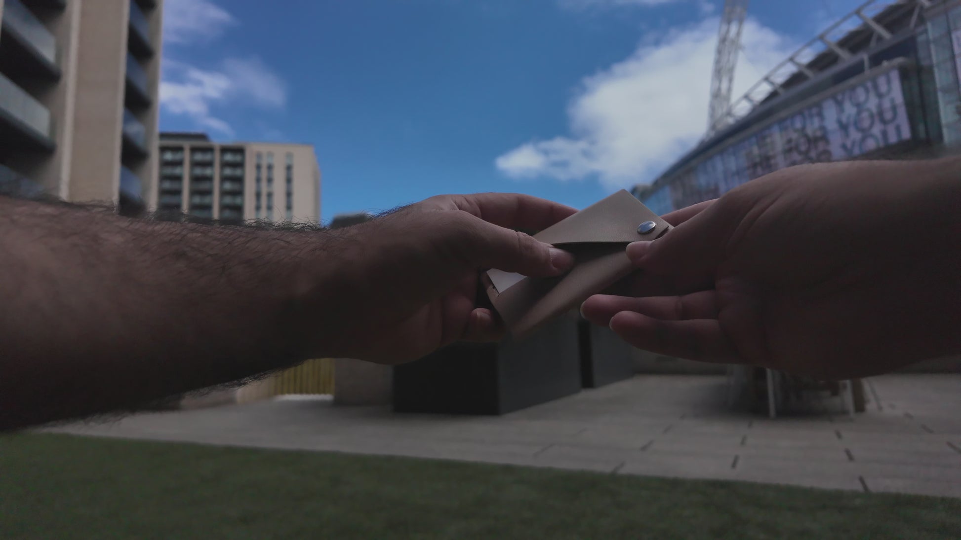 Beige leather envelope card holder demonstrated by hand in an outdoor urban setting near Wembley