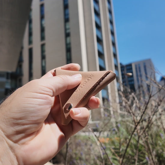 Hand holding a beige leather coin pouch outdoors on a bright sunny day