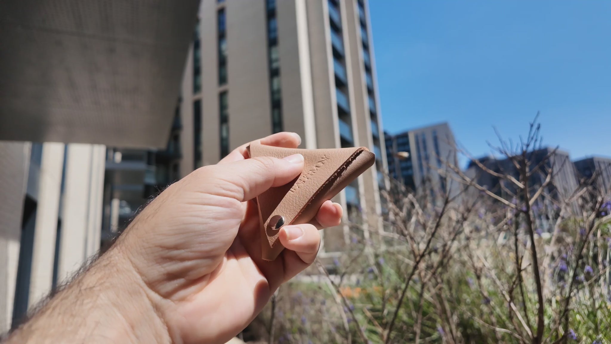 Hand holding a beige leather coin pouch outdoors on a bright sunny day