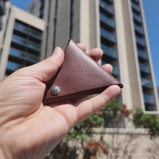 Handmade auburn leather coin pouch held outdoors in natural sunlight, highlighting its pebbled leather texture.