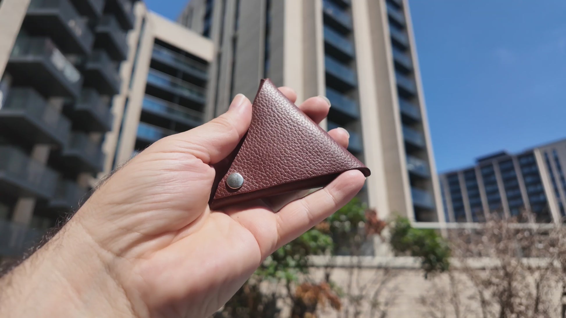 Handmade auburn leather coin pouch held outdoors in natural sunlight, highlighting its pebbled leather texture.