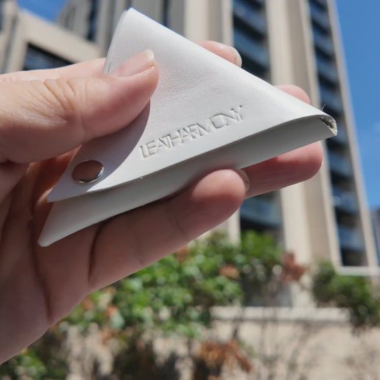 Handmade white leather coin pouch held outdoors in natural sunlight, showcasing the Leatharmony embossed logo.