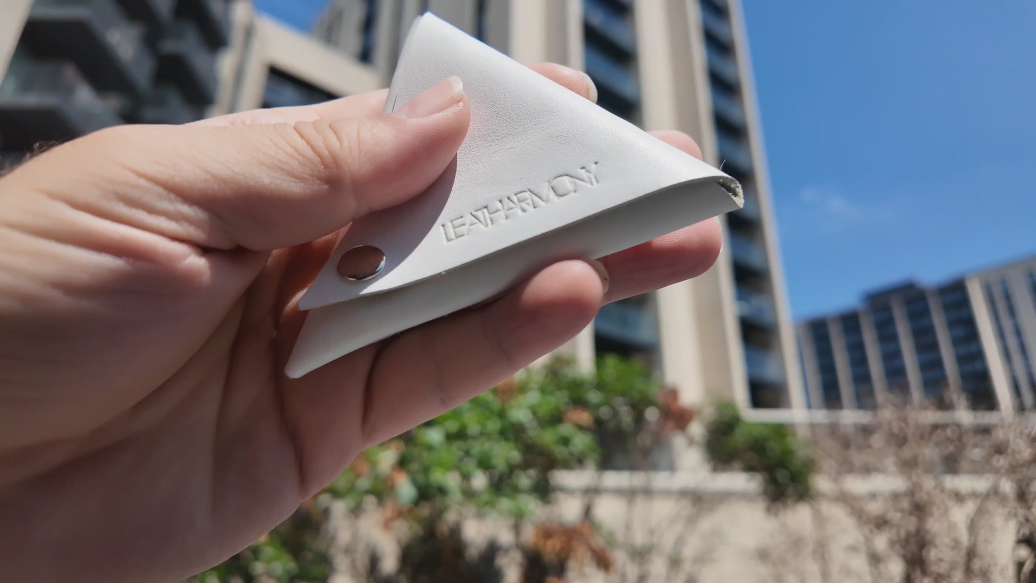 Handmade white leather coin pouch held outdoors in natural sunlight, showcasing the Leatharmony embossed logo.
