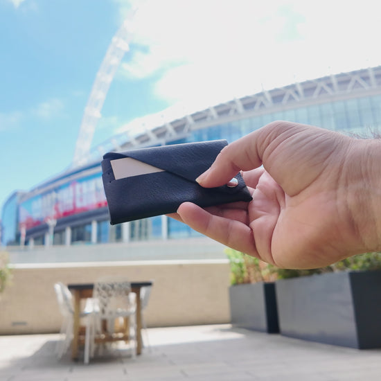 Black leather envelope card holder held outdoors in a modern urban setting near Wembley