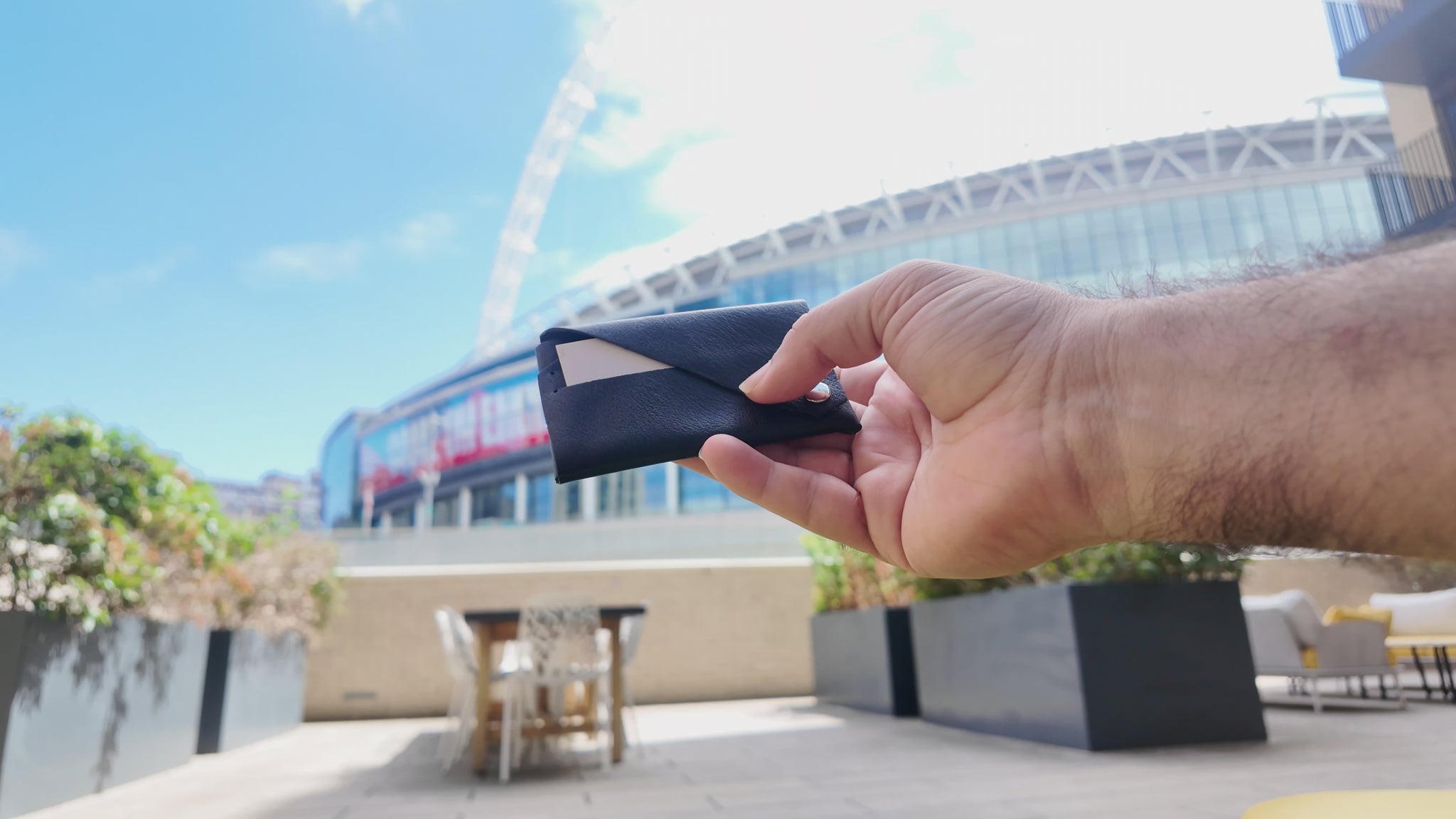 Black leather envelope card holder held outdoors in a modern urban setting near Wembley