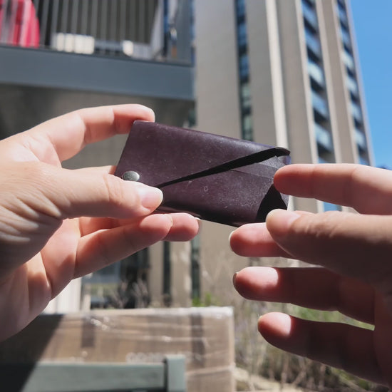 Burgundy patent leather card holder held in hand outdoors against a modern city background.