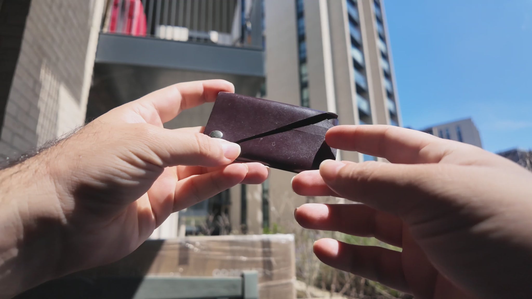Burgundy patent leather card holder held in hand outdoors against a modern city background.