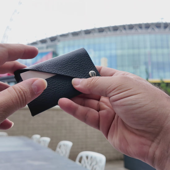 Black leather card holder held in both hands, showing its minimalist envelope-style design.