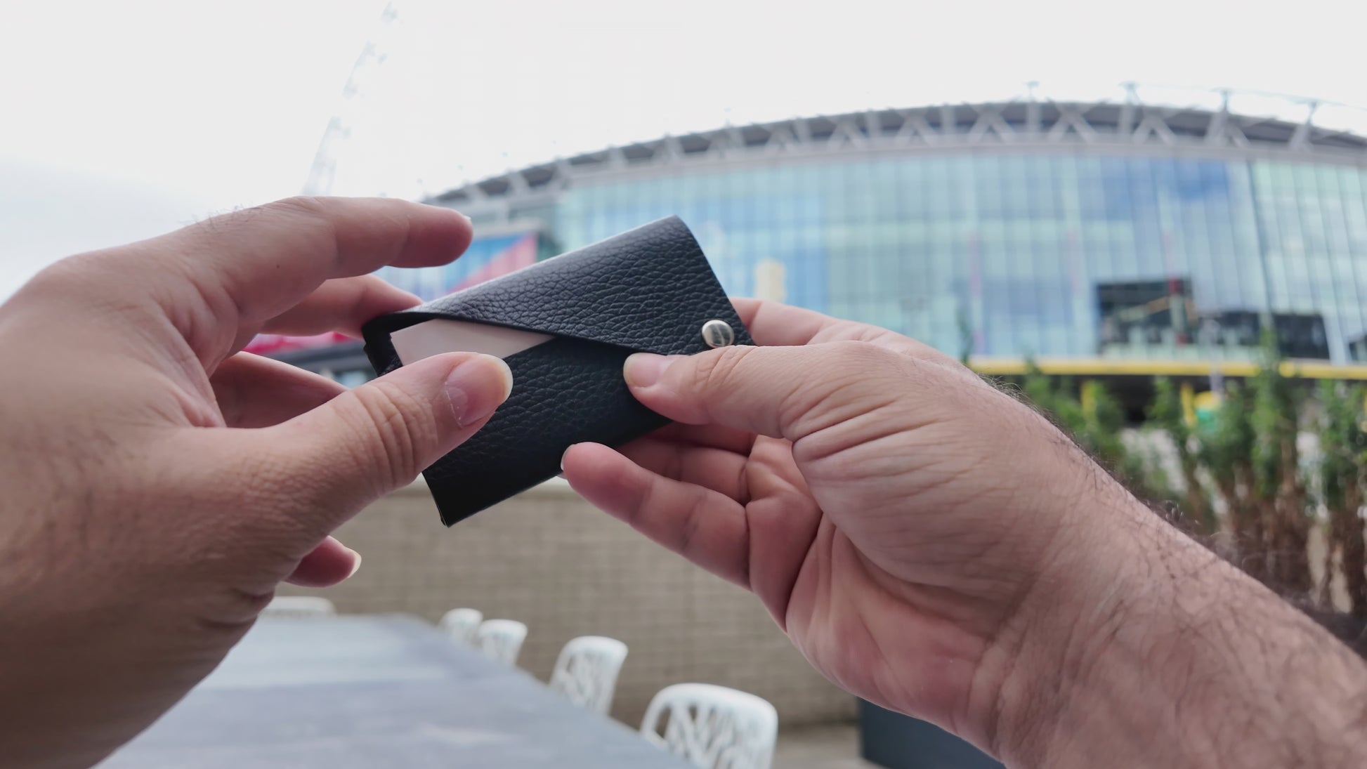 Black leather card holder held in both hands, showing its minimalist envelope-style design.