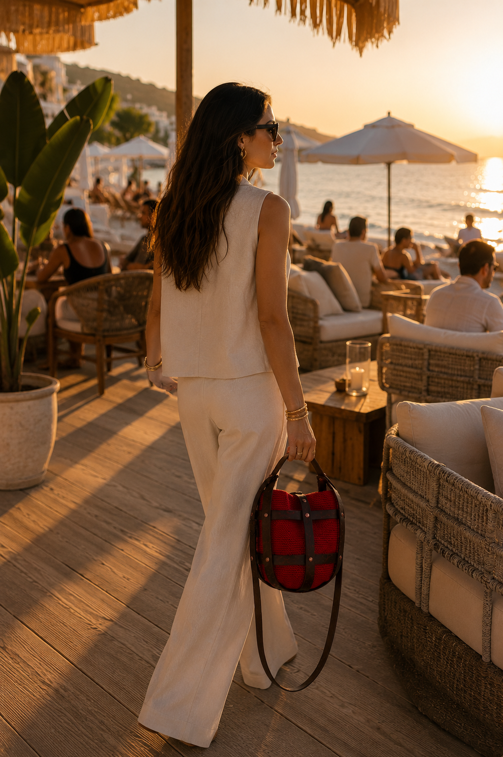 Woman carrying a handmade red crochet leather bag by hand at a luxury beach club during sunset.
