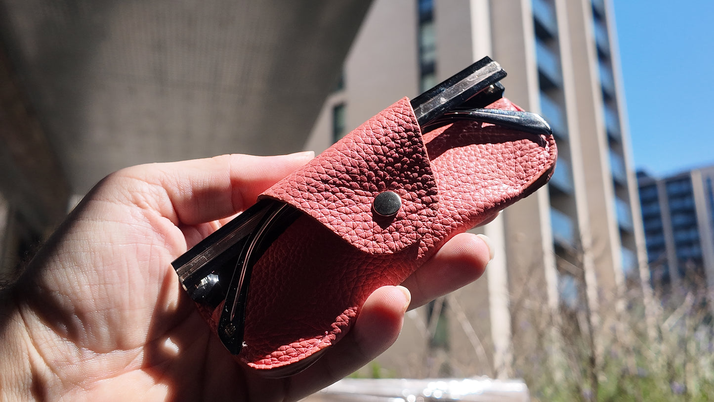 Close-up of a handmade salmon pink leather eyewear case holding sunglasses with detailed pebbled leather texture.