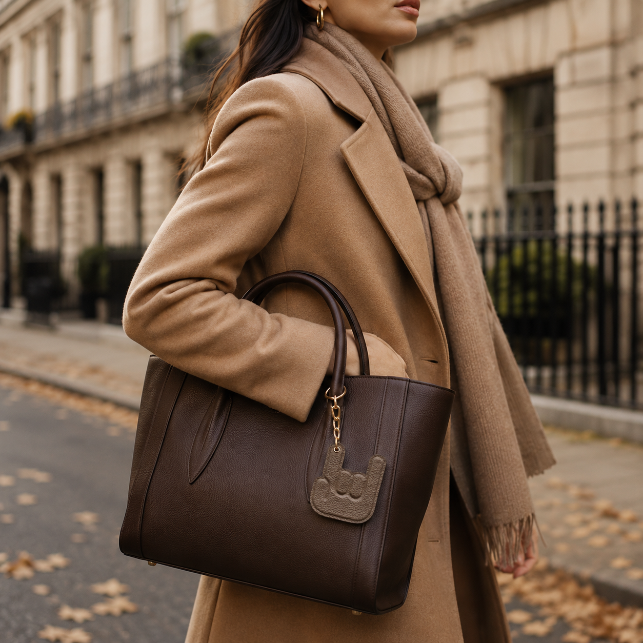 Handmade taupe leather keychain attached to a brown leather handbag carried on a city street.