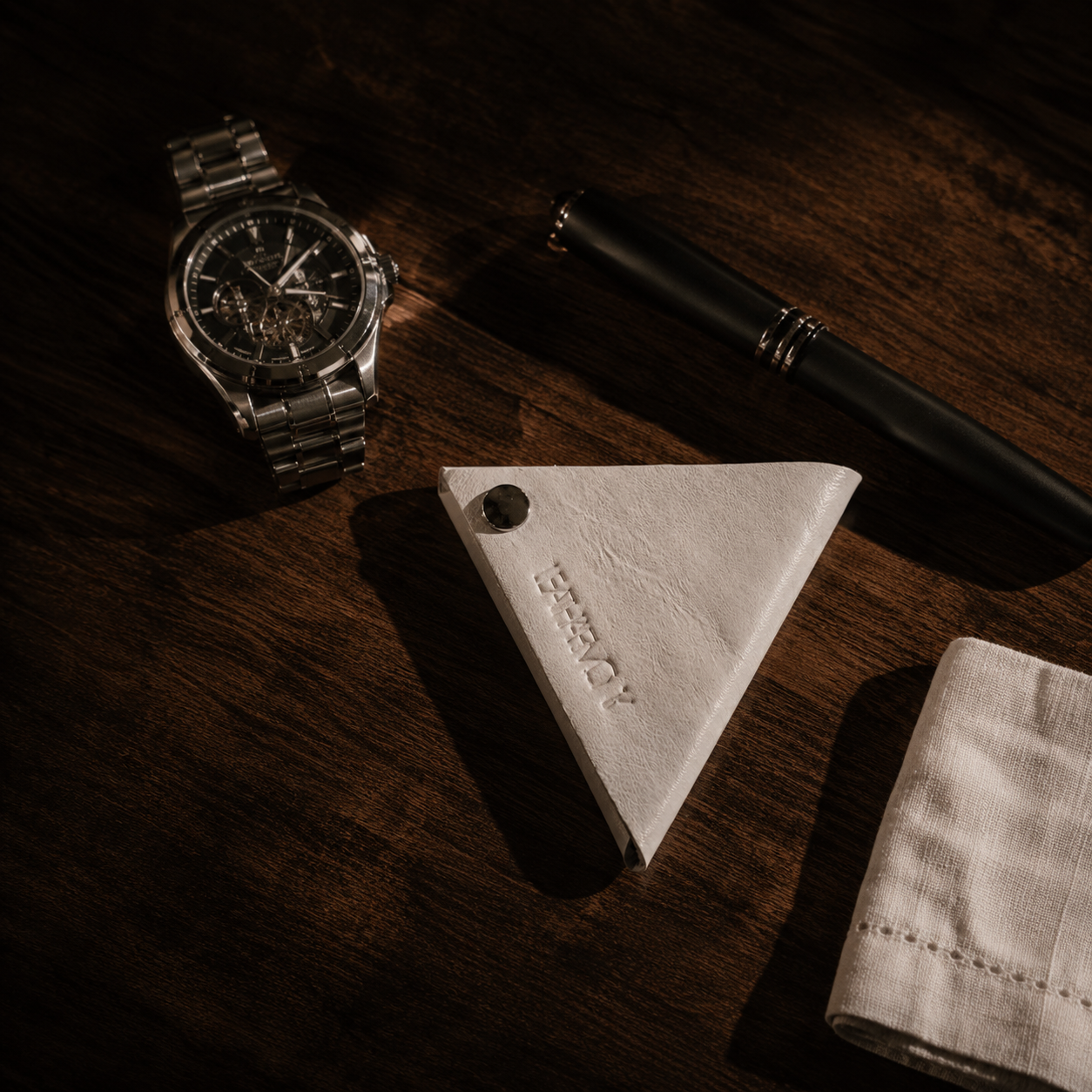 Handmade white genuine leather coin pouch displayed on a wooden desk with a luxury watch and pen.
