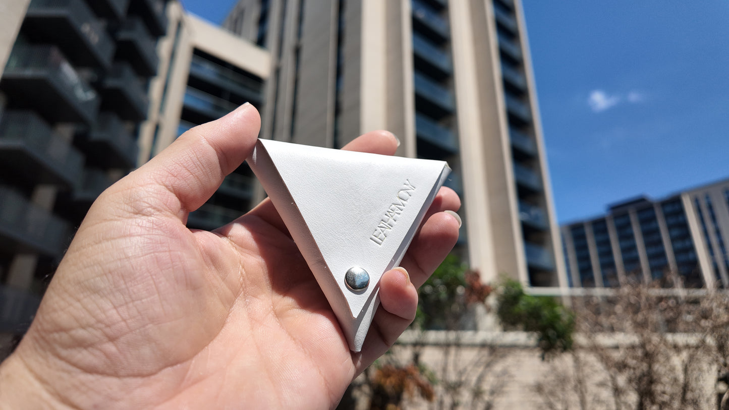 Front view of a white leather coin pouch photographed outdoors in bright natural daylight.