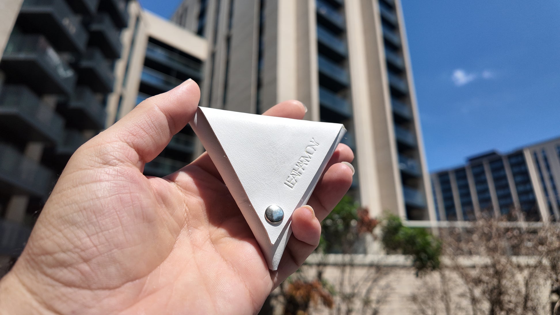 Front view of a white leather coin pouch photographed outdoors in bright natural daylight.